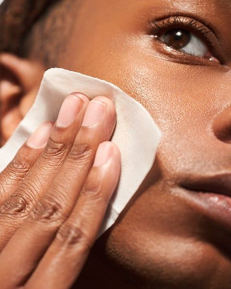Person cleaning their face with a white cloth against a neutral background